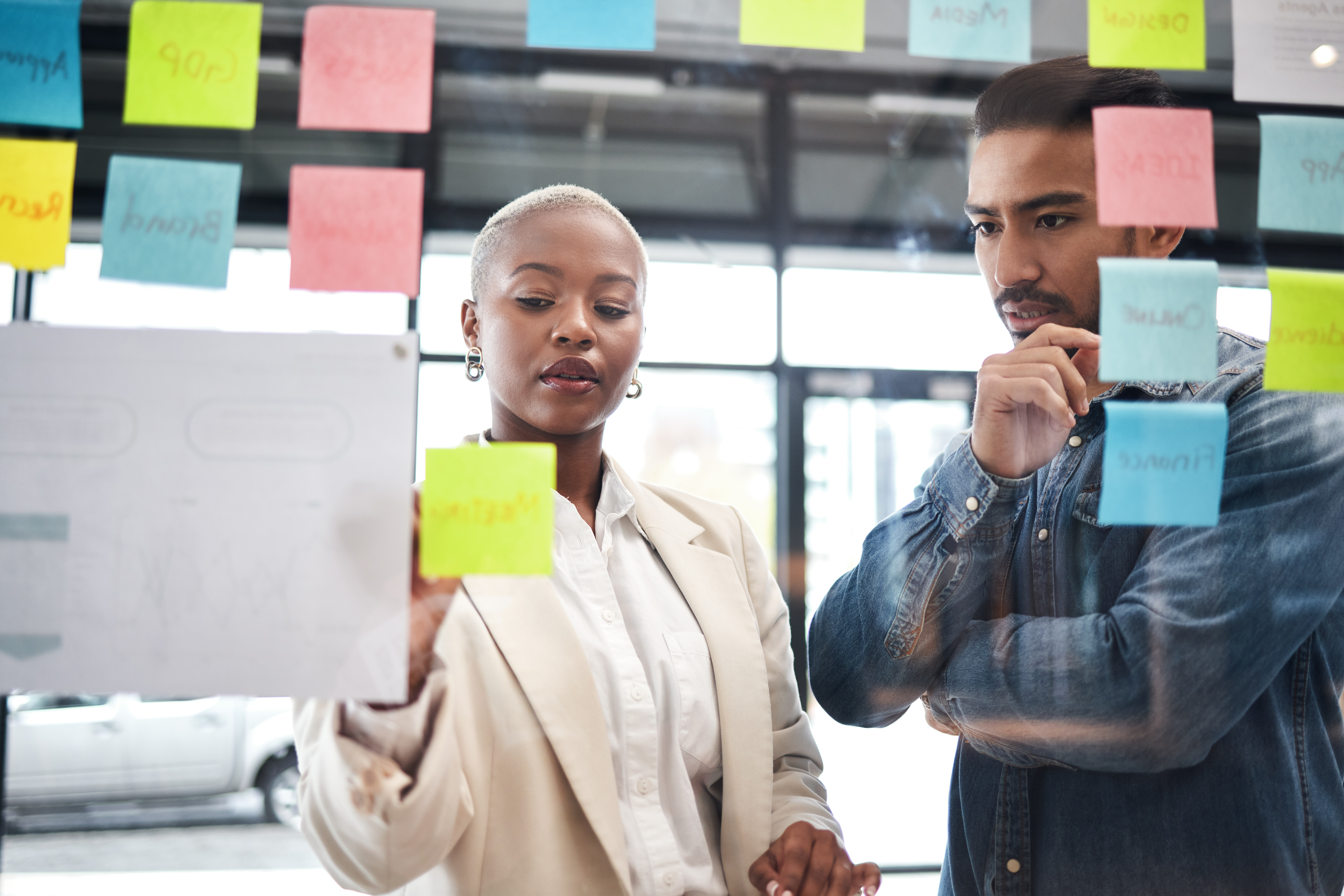 Two people discussing in front of a glass covered in sticky notes