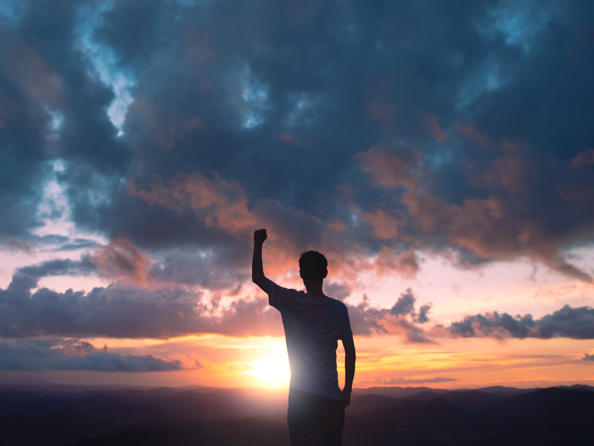 Standing man with fist raised in front of clouds.