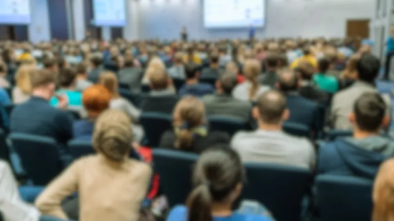 Rear view shot of seated audience in large conference hall slightly out of focus