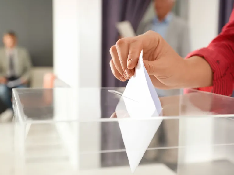 Hand putting ballot paper into box at polling station, closeup