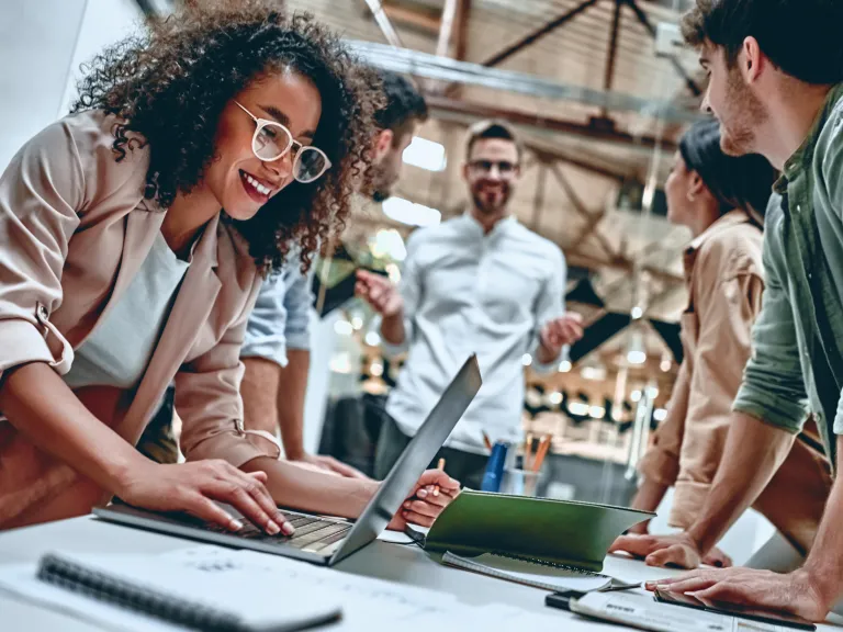 Close up of young professional woman working on laptop with colleagues